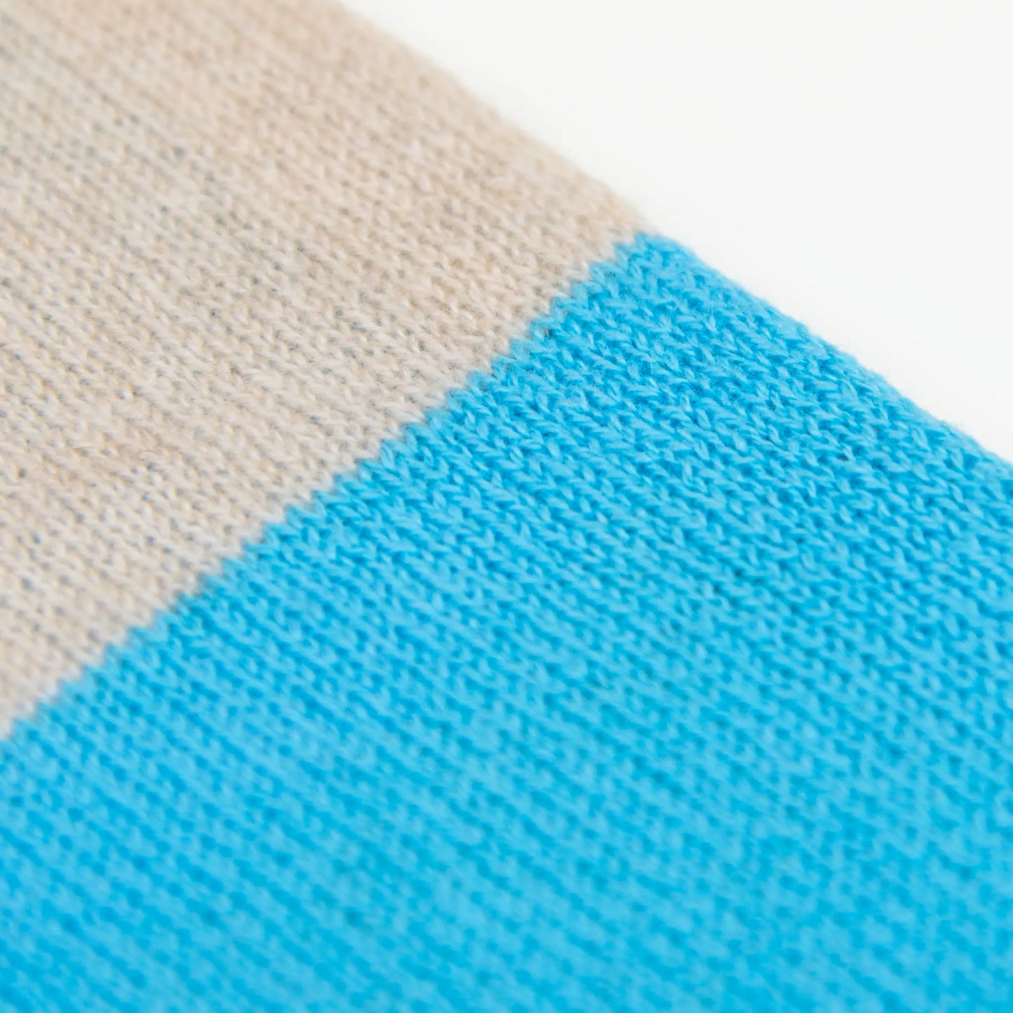 Dettaglio e texture tessuto della sciarpa in maglia 100% cashmere blu e beige, Made in Italy, realizzata su antichi telai. Grazie alla sua ampiezza, può essere utilizzata anche come stola. La pregiata fibra di cashmere offre un'eccezionale finezza e qualità termoisolanti, assicurando calore, protezione e leggerezza in tutte le stagioni. Un accessorio versatile, frutto della creatività di designer specializzati, che aggiunge eleganza e comfort al tuo look.