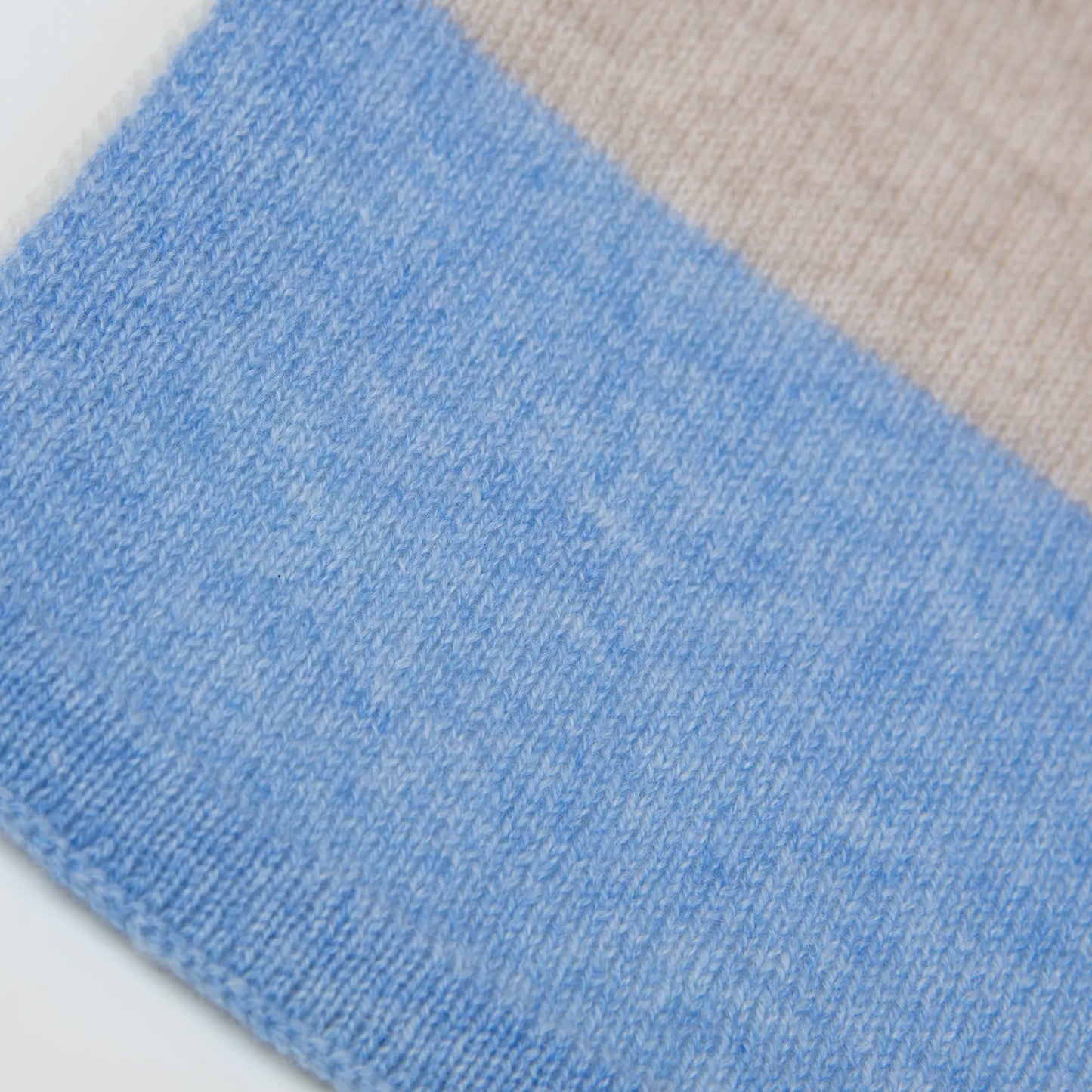 Dettaglio e texture tessuto della sciarpa in maglia 100% cashmere celeste, beige e grigia, Made in Italy, realizzata su antichi telai. Grazie alla sua ampiezza, può essere utilizzata anche come stola. La pregiata fibra di cashmere offre un'eccezionale finezza e qualità termoisolanti, assicurando calore, protezione e leggerezza in tutte le stagioni. Un accessorio versatile, frutto della creatività di designer specializzati, che aggiunge eleganza e comfort al tuo look.