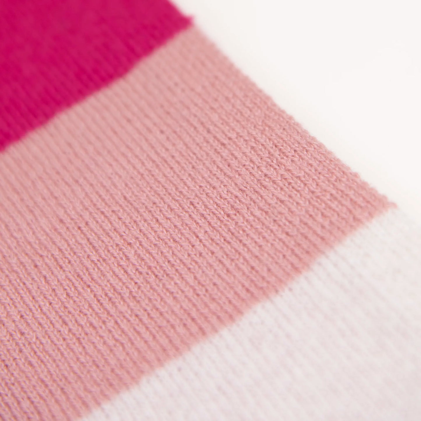Dettaglio e texture tessuto della sciarpa in maglia 100% cashmere rosa, viola e fucsia, Made in Italy, realizzata su antichi telai. Grazie alla sua ampiezza, può essere utilizzata anche come stola. La pregiata fibra di cashmere offre un'eccezionale finezza e qualità termoisolanti, assicurando calore, protezione e leggerezza in tutte le stagioni. Un accessorio versatile, frutto della creatività di designer specializzati, che aggiunge eleganza e comfort al tuo look.