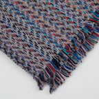 Dettaglio e texture tessuto della sciarpa in 100% cashmere di altissima qualità, Made in Italy, realizzata su telai in legno manuali degli anni '30. La base in vello di capra non colorato si intreccia con 100 fili di diverse tonalità, creando una profondità cromatica unica e un equilibrio armonioso di colori. Il risultato è un intreccio vibrante che esalta la morbidezza, la leggerezza e l'eleganza naturale del cashmere. Un accessorio raffinato, frutto della creatività di designer specializzati.