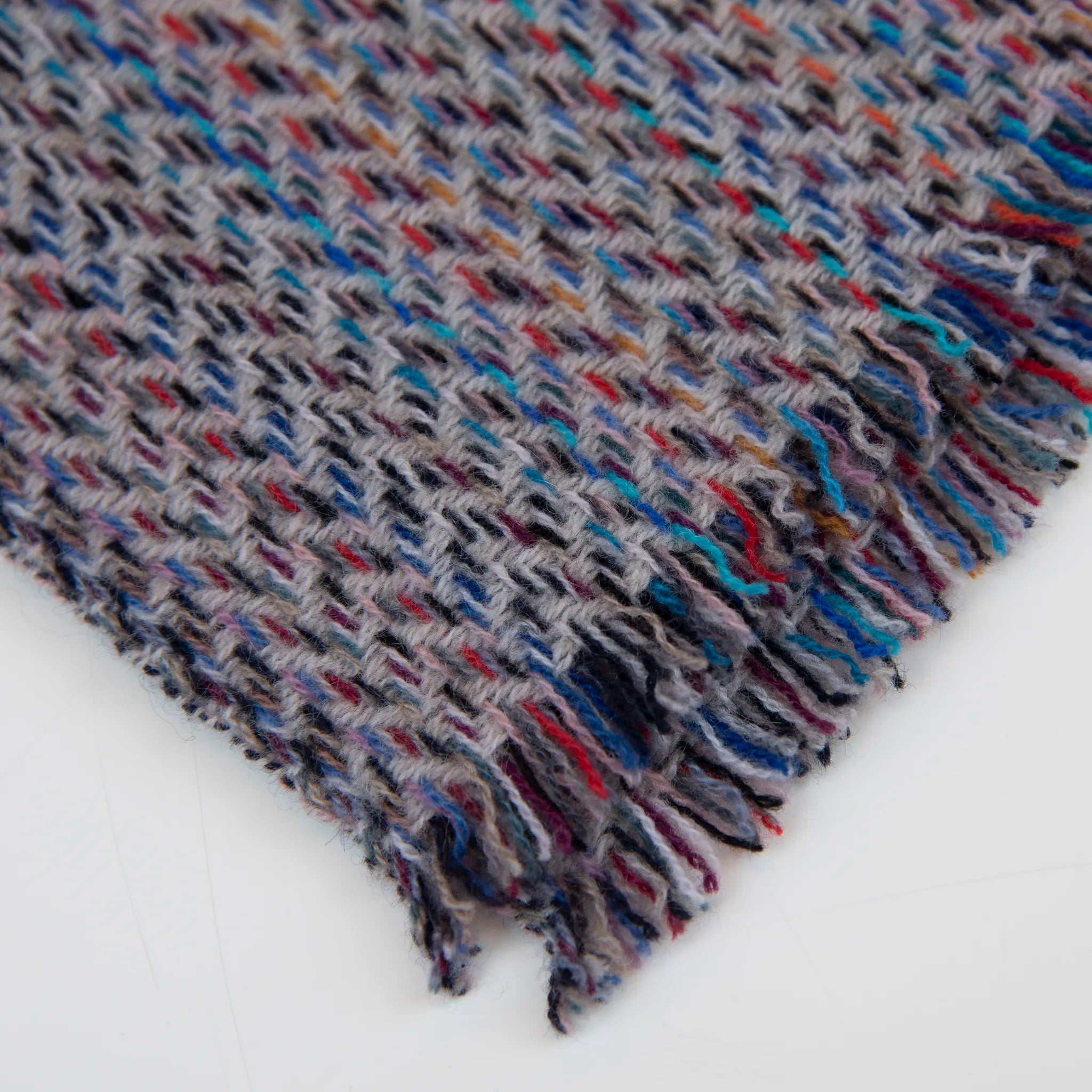 Dettaglio e texture tessuto della sciarpa in 100% cashmere di altissima qualità, Made in Italy, realizzata su telai in legno manuali degli anni '30. La base in vello di capra non colorato si intreccia con 100 fili di diverse tonalità, creando una profondità cromatica unica e un equilibrio armonioso di colori. Il risultato è un intreccio vibrante che esalta la morbidezza, la leggerezza e l'eleganza naturale del cashmere. Un accessorio raffinato, frutto della creatività di designer specializzati.