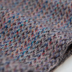 Dettaglio e texture tessuto della sciarpa in 100% cashmere di altissima qualità, Made in Italy, realizzata su telai in legno manuali degli anni '30. La base in vello di capra non colorato si intreccia con 100 fili di diverse tonalità, creando una profondità cromatica unica e un equilibrio armonioso di colori. Il risultato è un intreccio vibrante che esalta la morbidezza, la leggerezza e l'eleganza naturale del cashmere. Un accessorio raffinato, frutto della creatività di designer specializzati.
