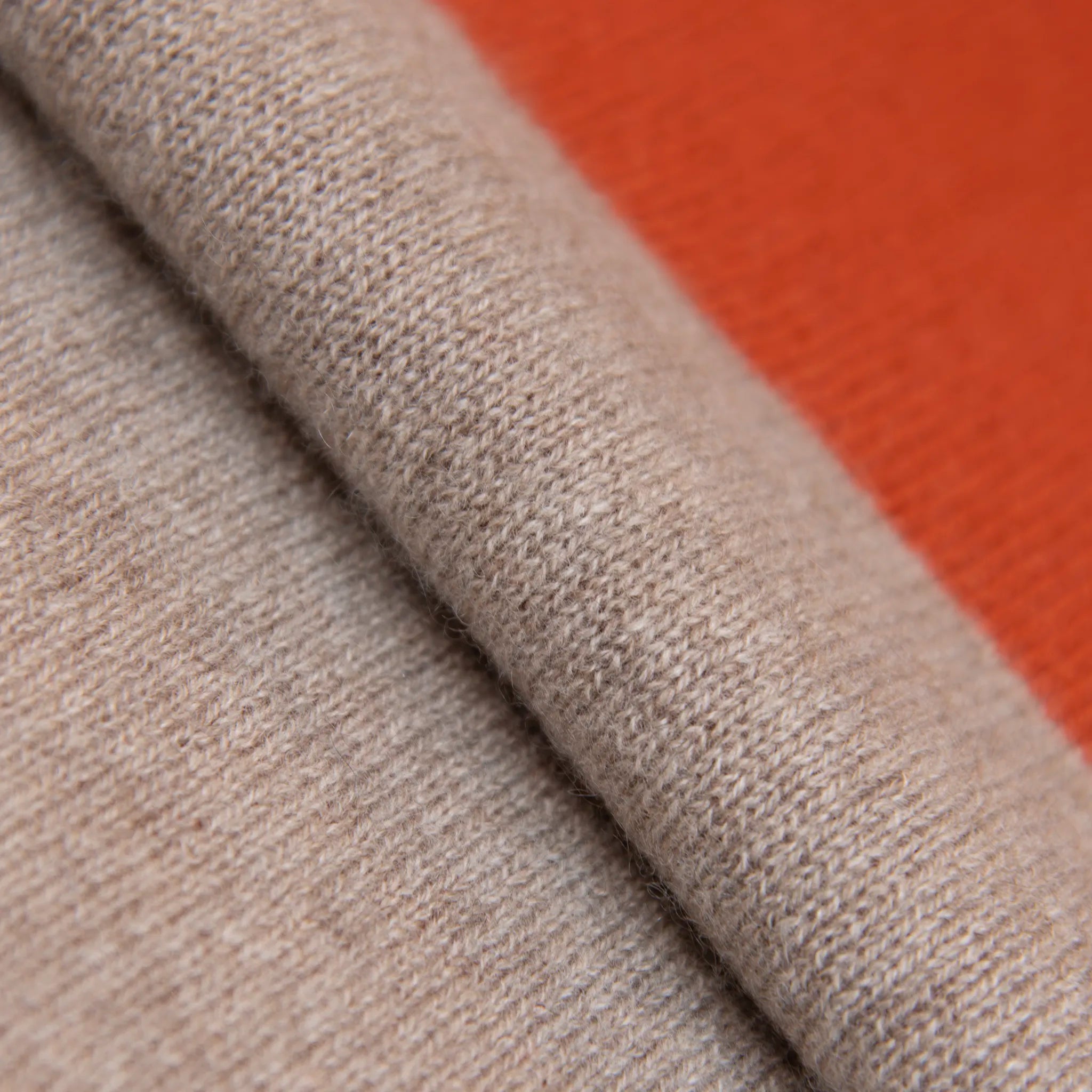 Dettaglio e texture tessuto della sciarpa in maglia 100% cashmere arancio e beige, Made in Italy, realizzata su antichi telai. Grazie alla sua ampiezza, può essere utilizzata anche come stola. La pregiata fibra di cashmere offre un'eccezionale finezza e qualità termoisolanti, assicurando calore, protezione e leggerezza in tutte le stagioni. Un accessorio versatile, frutto della creatività di designer specializzati, che aggiunge eleganza e comfort al tuo look.