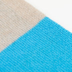 Dettaglio e texture tessuto della sciarpa in maglia 100% cashmere blu e beige, Made in Italy, realizzata su antichi telai. Grazie alla sua ampiezza, può essere utilizzata anche come stola. La pregiata fibra di cashmere offre un'eccezionale finezza e qualità termoisolanti, assicurando calore, protezione e leggerezza in tutte le stagioni. Un accessorio versatile, frutto della creatività di designer specializzati, che aggiunge eleganza e comfort al tuo look.