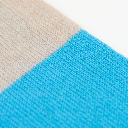 Dettaglio e texture tessuto della sciarpa in maglia 100% cashmere blu e beige, Made in Italy, realizzata su antichi telai. Grazie alla sua ampiezza, può essere utilizzata anche come stola. La pregiata fibra di cashmere offre un'eccezionale finezza e qualità termoisolanti, assicurando calore, protezione e leggerezza in tutte le stagioni. Un accessorio versatile, frutto della creatività di designer specializzati, che aggiunge eleganza e comfort al tuo look.