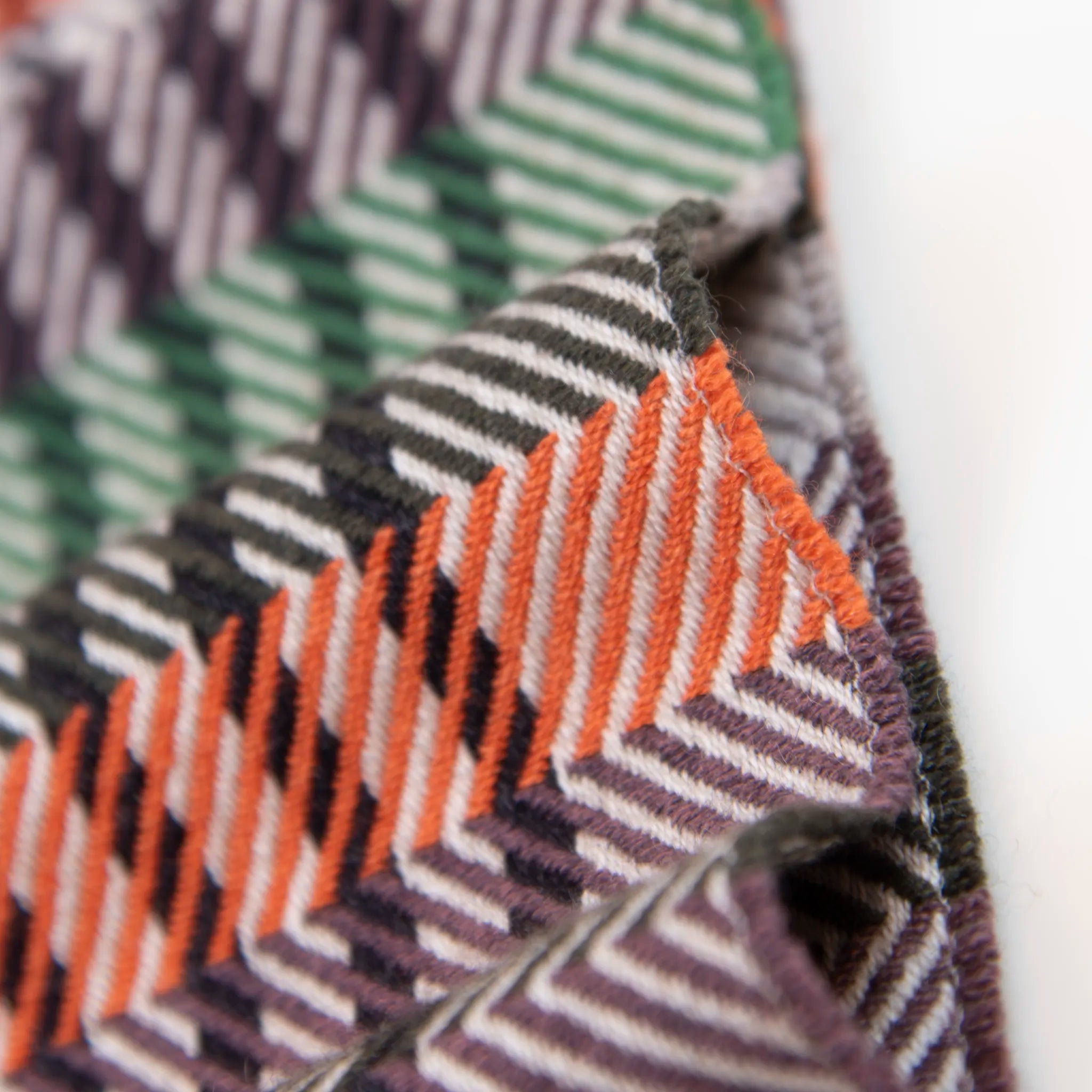 Dettaglio e texture tessuto della sciarpa in cashmere e seta, arancio, viola, verde, Made in Italy, con pattern a righe trasversali che dona dinamismo visivo. La fusione armoniosa dei colori rende questa sciarpa facile da abbinare in ogni occasione, offrendo una sensazione di morbidezza, calore e leggerezza. Un accessorio raffinato, frutto della creatività di designer esperti, perfetto per ogni look.