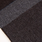 Dettaglio e texture tessuto della sciarpa in cashmere e seta, marrone e grigia, Made in Italy, con accostamento di due pattern intramontabili: riga e spinato. Curata nei minimi dettagli, offre straordinaria morbidezza e un comfort avvolgente, rendendola un accessorio elegante e versatile.