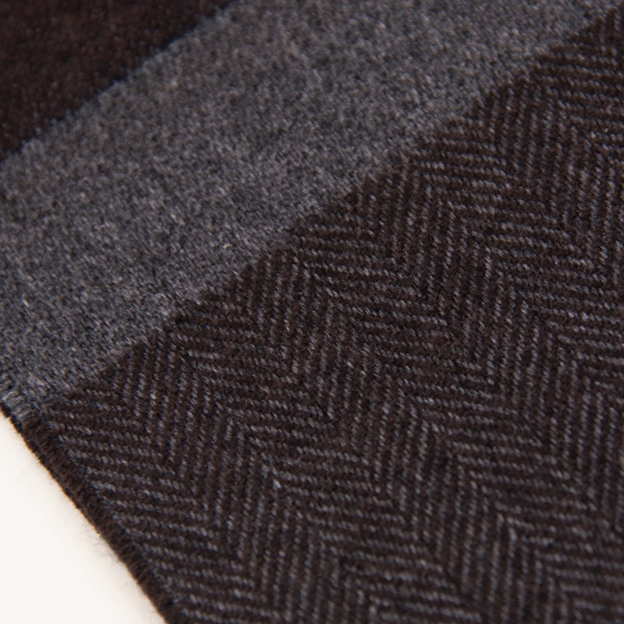 Dettaglio e texture tessuto della sciarpa in cashmere e seta, marrone e grigia, Made in Italy, con accostamento di due pattern intramontabili: riga e spinato. Curata nei minimi dettagli, offre straordinaria morbidezza e un comfort avvolgente, rendendola un accessorio elegante e versatile.