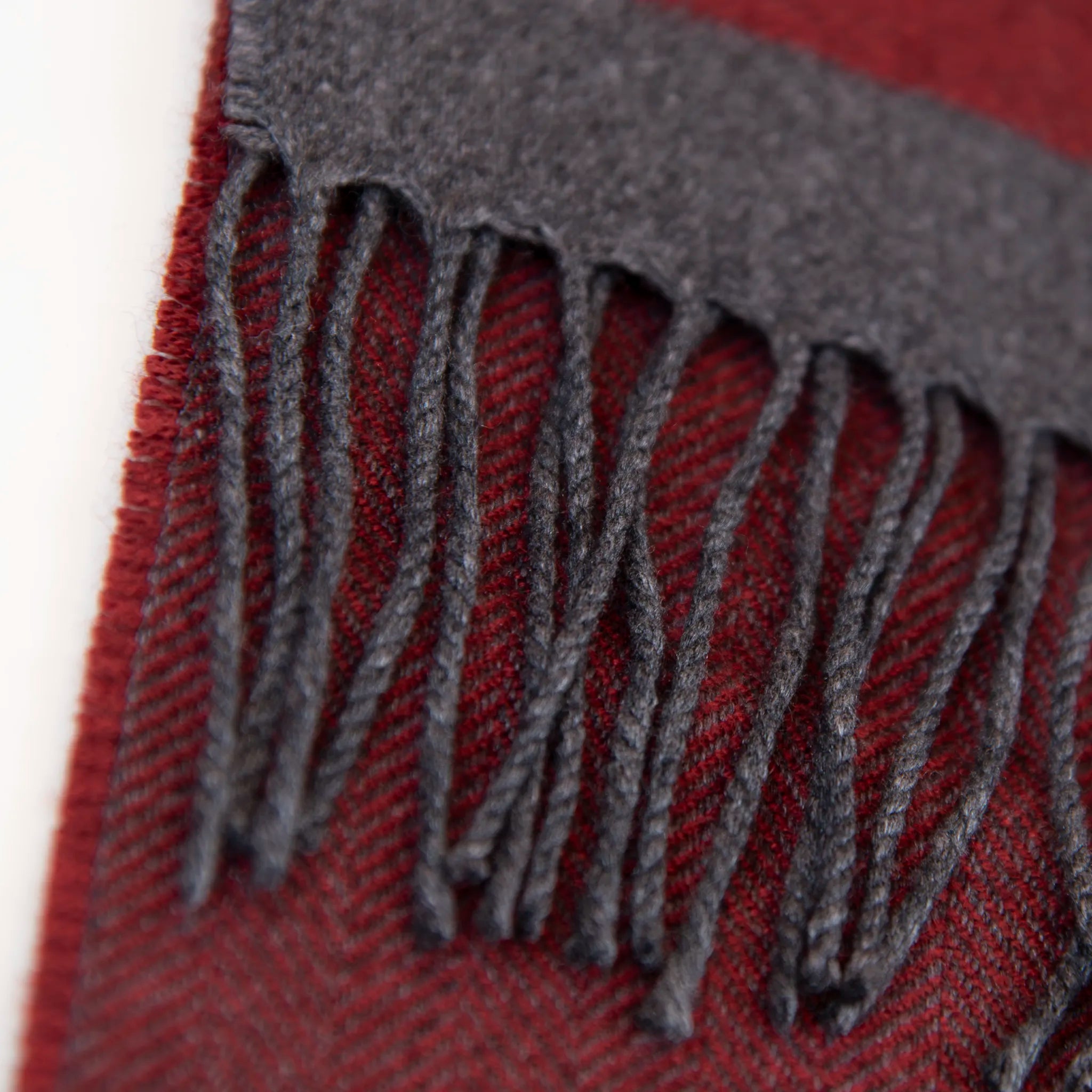 Dettaglio e texture tessuto della sciarpa in cashmere e seta, rossa e grigia, Made in Italy, con accostamento di due pattern intramontabili: riga e spinato. Curata nei minimi dettagli, offre straordinaria morbidezza e un comfort avvolgente, rendendola un accessorio elegante e versatile.
