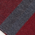 Dettaglio e texture tessuto della sciarpa in cashmere e seta, rossa e grigia, Made in Italy, con accostamento di due pattern intramontabili: riga e spinato. Curata nei minimi dettagli, offre straordinaria morbidezza e un comfort avvolgente, rendendola un accessorio elegante e versatile.