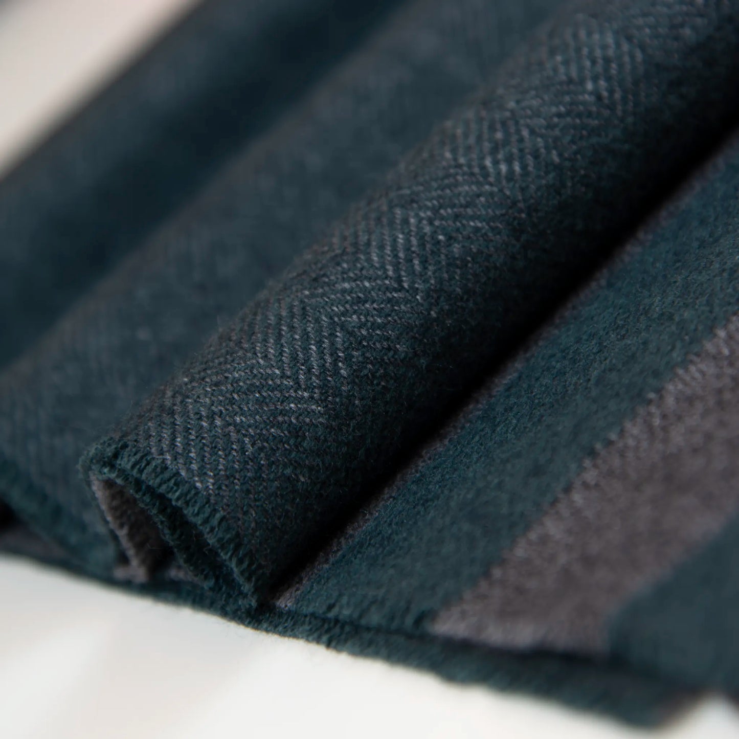 Dettaglio e texture tessuto della sciarpa in cashmere e seta, verde e grigia, Made in Italy, con accostamento di due pattern intramontabili: riga e spinato. Curata nei minimi dettagli, offre straordinaria morbidezza e un comfort avvolgente, rendendola un accessorio elegante e versatile.