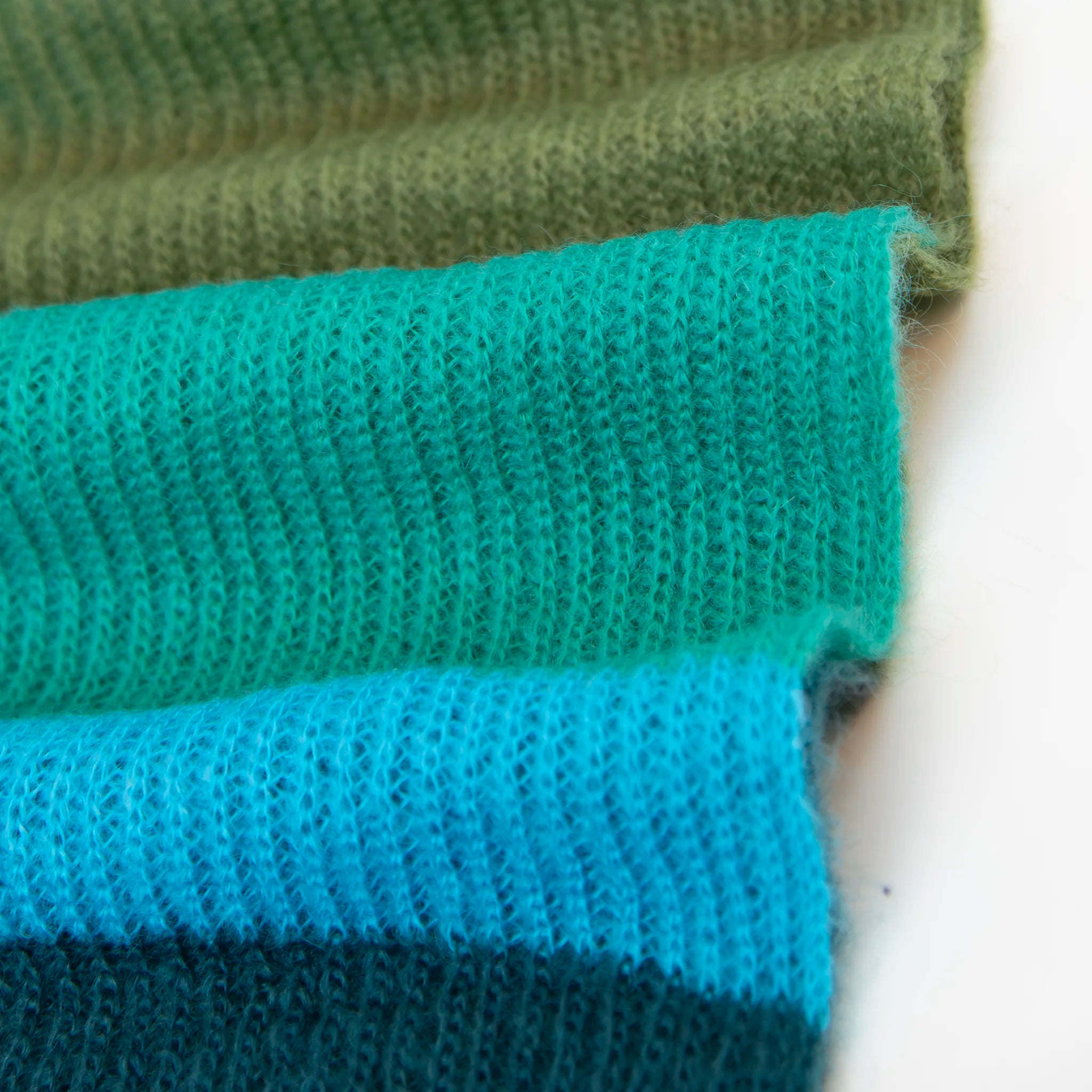 Dettaglio e texture tessuto della Sciarpa in lana mohair, verde,  Made in Italy, realizzata nel più antico lanificio della Calabria su telai degli anni '30, garantendo qualità e durata nel tempo. I colori ispirati al sottobosco autunnale dell'Appennino Silano evocano la quiete e la bellezza dei paesaggi autunnali. Morbida al tatto, offre una sensazione di sofficità che avvolge delicatamente il corpo, per un comfort senza pari.