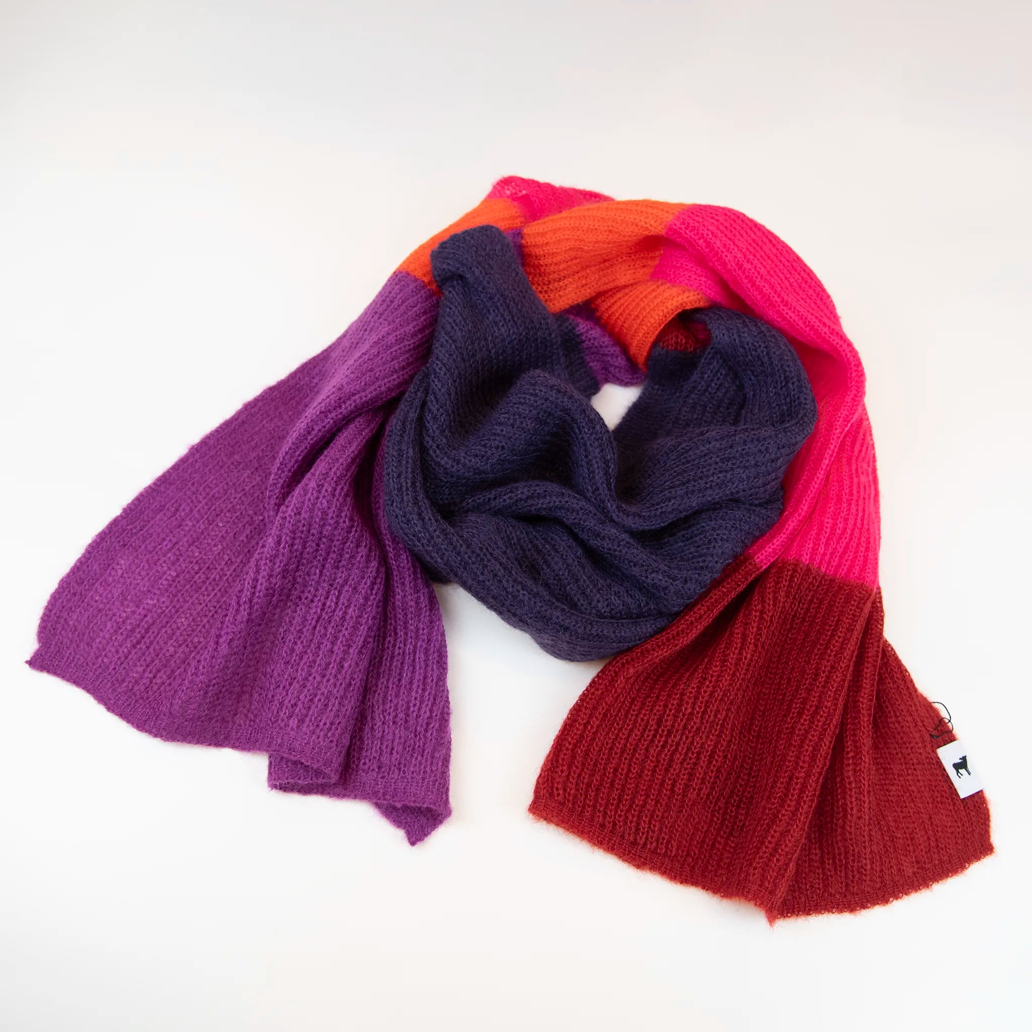 Sciarpa in lana mohair viola, fucsia, arancio, Made in Italy, realizzata nel più antico lanificio della Calabria su telai degli anni '30, garantendo qualità e durata nel tempo. I colori ispirati ai frutti rossi dei boschi evocano calore e naturale bellezza. Morbida al tatto, offre una sensazione di sofficità che avvolge delicatamente il corpo, per un comfort senza pari.