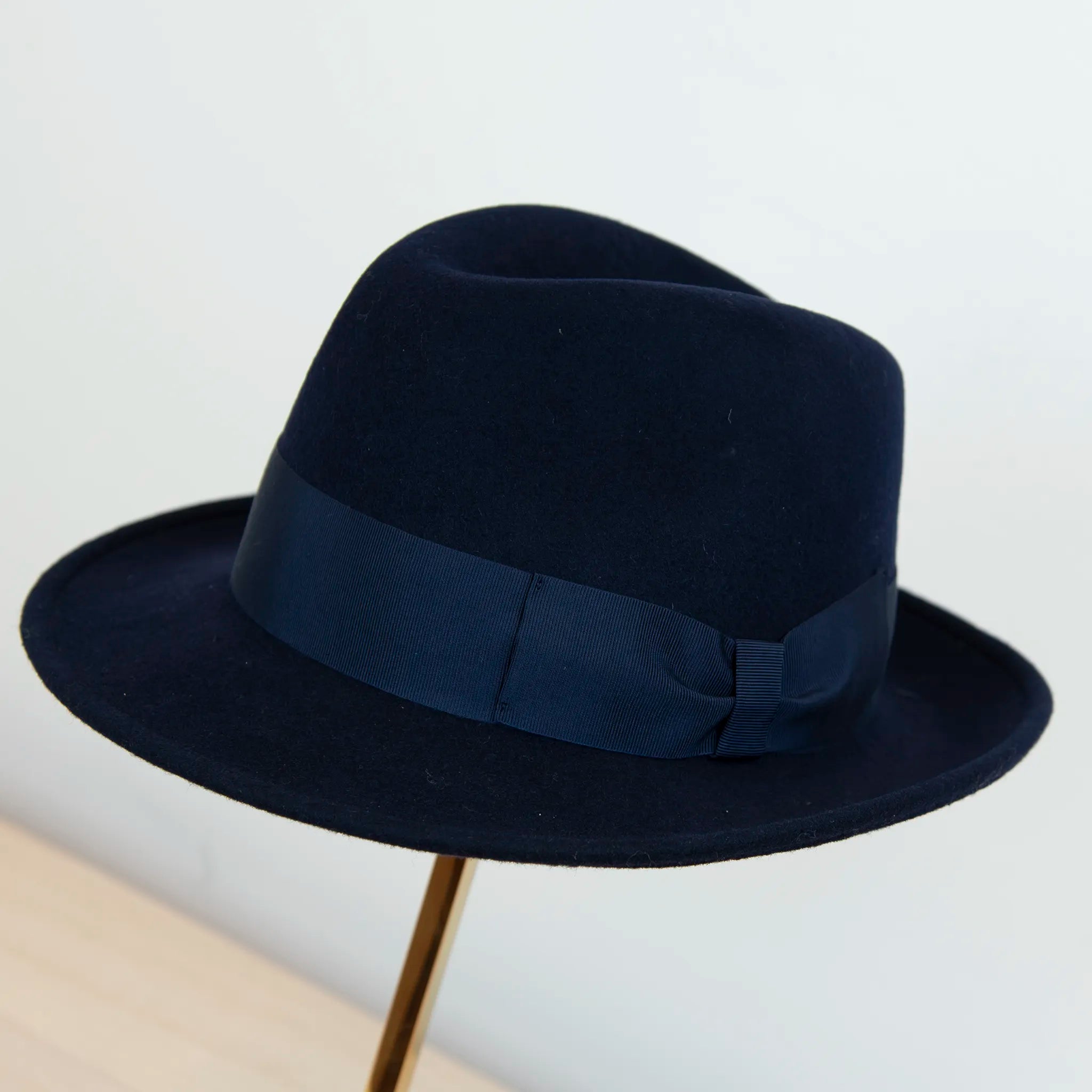 Cappello in feltro di lana blu Made in Italy, ispirato a Humphrey Bogart. Falda media 5,5 cm rialzata sul retro, cupola 11,5 cm, cinta in gros-grain 4 cm blu. Eleganza senza tempo.
