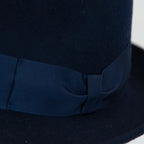 Dettaglio cinta e tessuto del cappello in feltro di lana blu, Made in Italy, ispirato a Humphrey Bogart. Falda media 5,5 cm rialzata sul retro, cupola 11,5 cm, cinta in gros-grain 4 cm blu. Eleganza senza tempo.