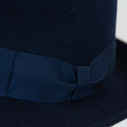 Dettaglio cinta e tessuto del cappello in feltro di lana blu, Made in Italy, ispirato a Humphrey Bogart. Falda media 5,5 cm rialzata sul retro, cupola 11,5 cm, cinta in gros-grain 4 cm blu. Eleganza senza tempo.