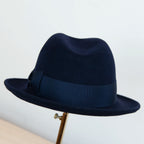 Cappello in feltro di lana blu, Made in Italy, ispirato a Humphrey Bogart. Falda media 5,5 cm rialzata sul retro, cupola 11,5 cm, cinta in gros-grain 4 cm blu. Eleganza senza tempo.