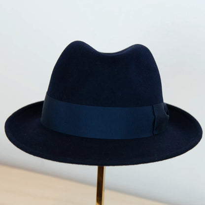 Dettaglio del cappello in feltro di lana blu, Made in Italy, ispirato a Humphrey Bogart. Falda media 5,5 cm rialzata sul retro, cupola 11,5 cm, cinta in gros-grain 4 cm blu. Eleganza senza tempo.