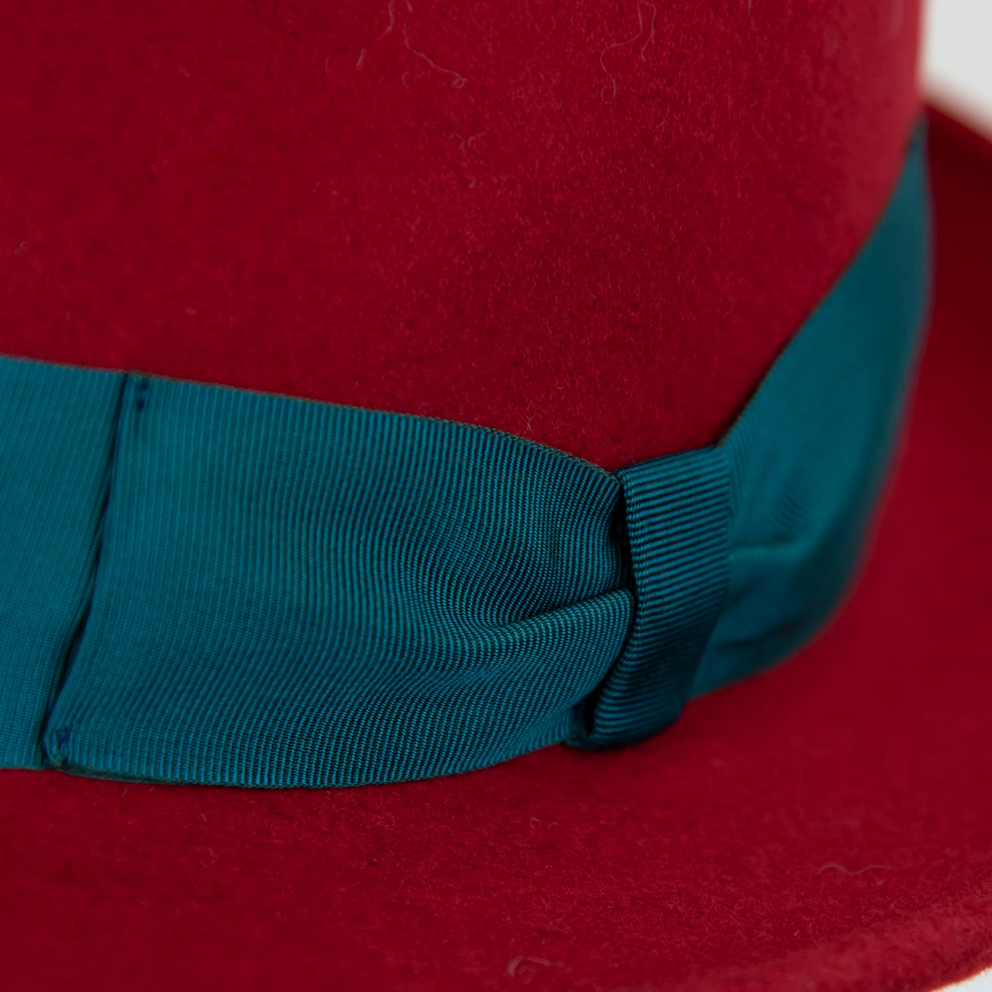 Dettaglio e tessuto del cappello in feltro di lana rosso, Made in Italy, ispirato a Humphrey Bogart. Falda media 5,5 cm rialzata sul retro, cupola 11,5 cm, cinta in gros-grain 4 cm verde. Eleganza senza tempo.