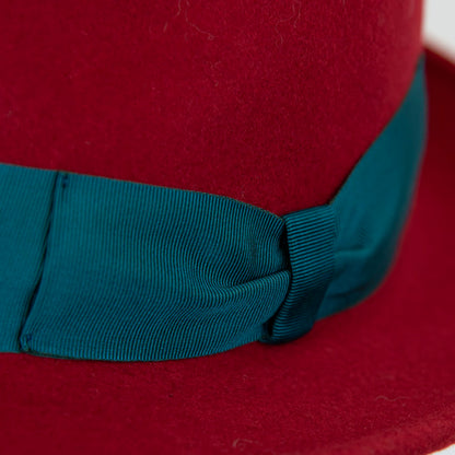 Dettaglio e tessuto del cappello in feltro di lana rosso, Made in Italy, ispirato a Humphrey Bogart. Falda media 5,5 cm rialzata sul retro, cupola 11,5 cm, cinta in gros-grain 4 cm verde. Eleganza senza tempo.