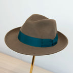 Cappello in feltro di lana marrone Made in Italy, ispirato a Humphrey Bogart. Falda media 5,5 cm rialzata sul retro, cupola 11,5 cm, cinta in gros-grain 4 cm verde. Eleganza senza tempo.