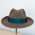 Cappello in feltro di lana marrone Made in Italy, ispirato a Humphrey Bogart. Falda media 5,5 cm rialzata sul retro, cupola 11,5 cm, cinta in gros-grain 4 cm verde. Eleganza senza tempo.