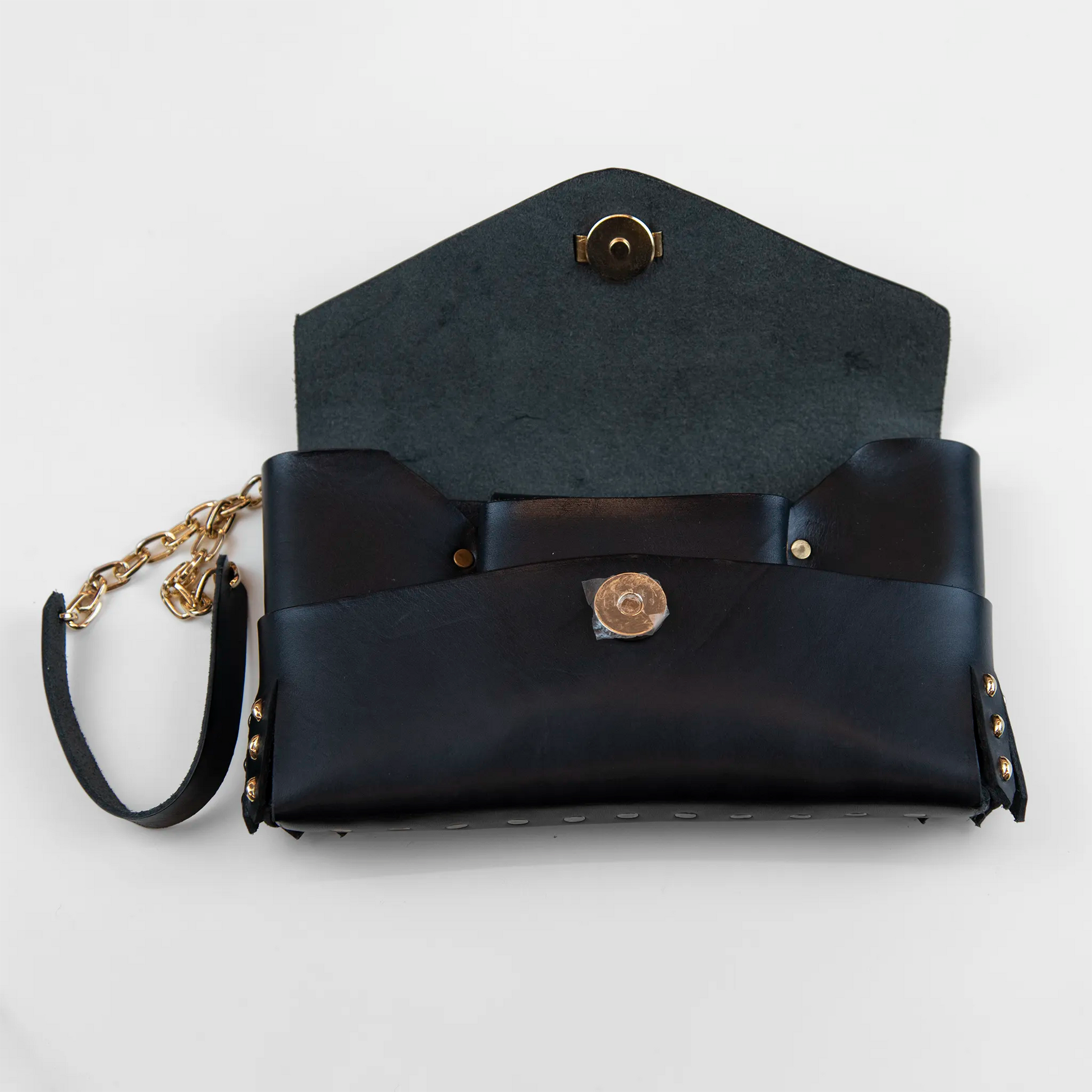 Portatutto in pelle nero borchiato con chiusura a calamita e polsiera per facile trasporto. Made in Italy, realizzato senza cuciture, secondo la tradizione degli antichi sellai Toscani, per maggiore robustezza e durata.