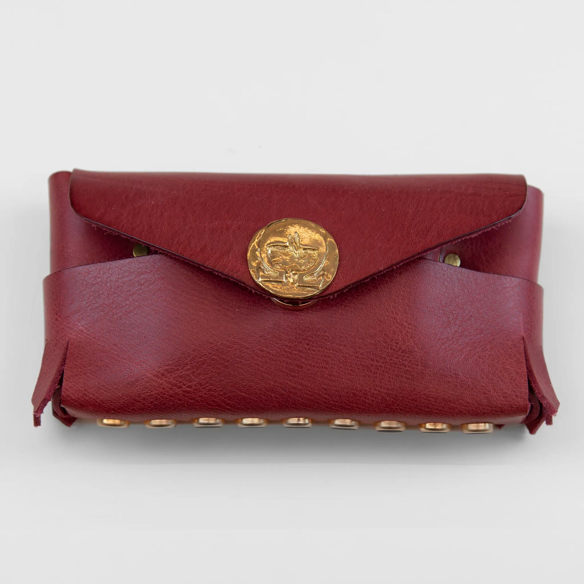 Portatutto in pelle rosso borchiato con chiusura a calamita, Made in Italy, realizzato interamente a mano senza cuciture secondo la tradizione degli antichi sellai Toscani, per una maggiore robustezza e durata nel tempo.