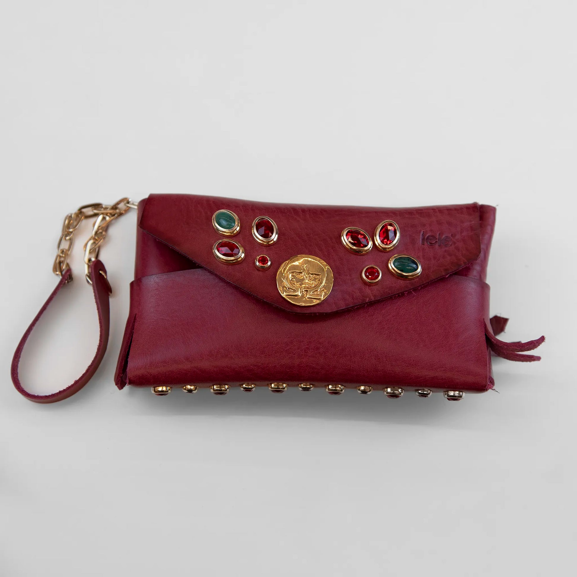 Portatutto in pelle rosso borchiato con pietre colorate, chiusura a calamita e polsiera per un pratico trasporto. Made in Italy, realizzato interamente a mano senza cuciture secondo la tradizione degli antichi sellai Toscani, per maggiore robustezza e durata nel tempo.