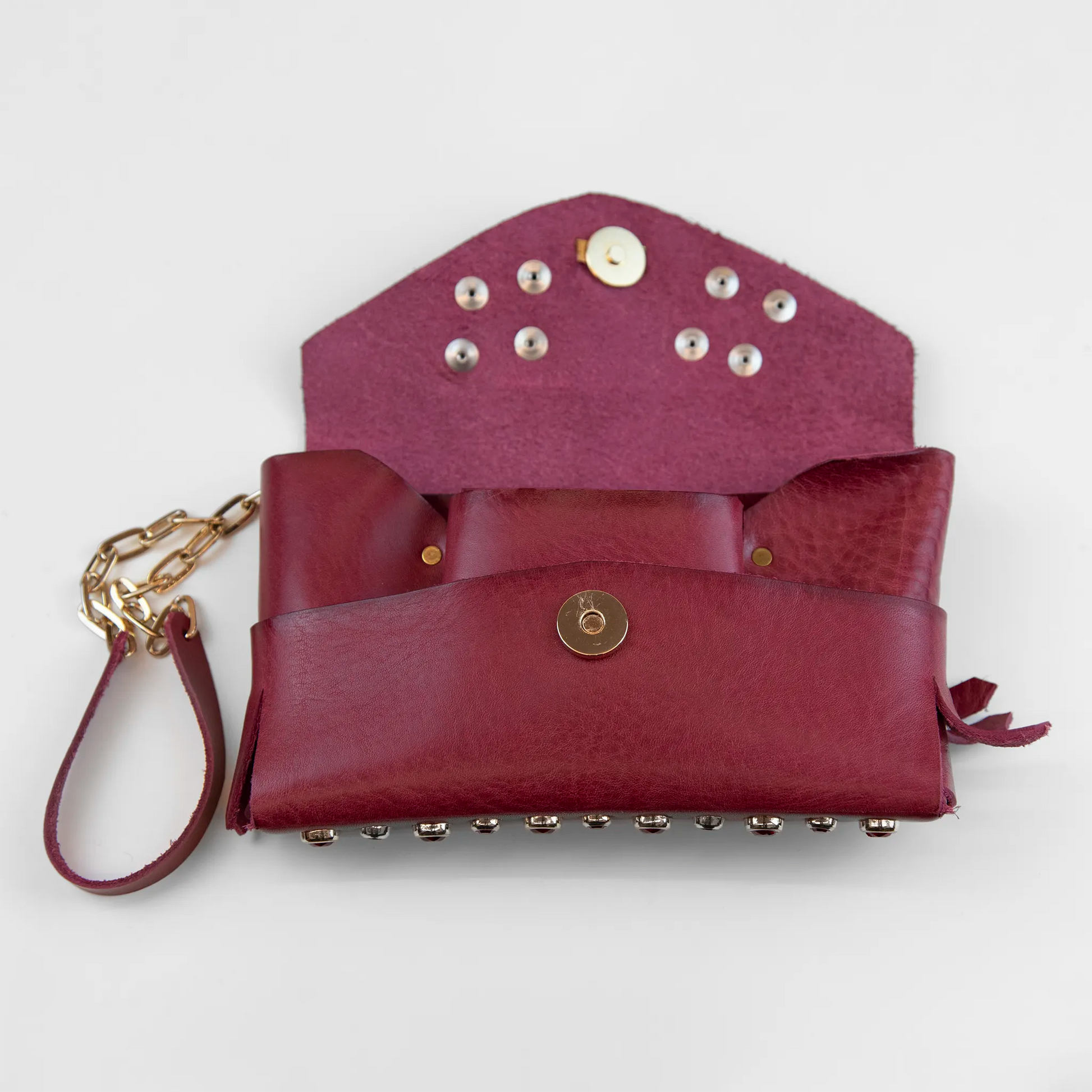 Portatutto in pelle rosso borchiato con pietre colorate, chiusura a calamita e polsiera per un pratico trasporto. Made in Italy, realizzato interamente a mano senza cuciture secondo la tradizione degli antichi sellai Toscani, per maggiore robustezza e durata nel tempo.