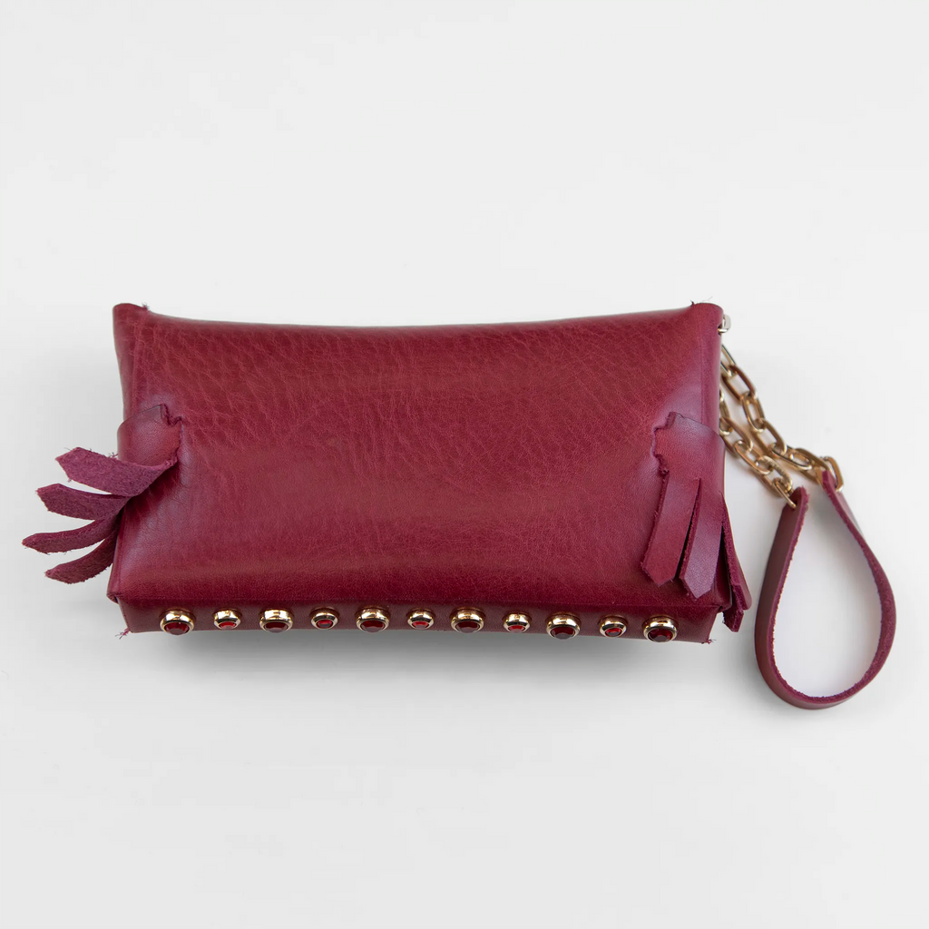 Portatutto in pelle rosso borchiato con pietre colorate, chiusura a calamita e polsiera per un pratico trasporto. Made in Italy, realizzato interamente a mano senza cuciture secondo la tradizione degli antichi sellai Toscani, per maggiore robustezza e durata nel tempo.