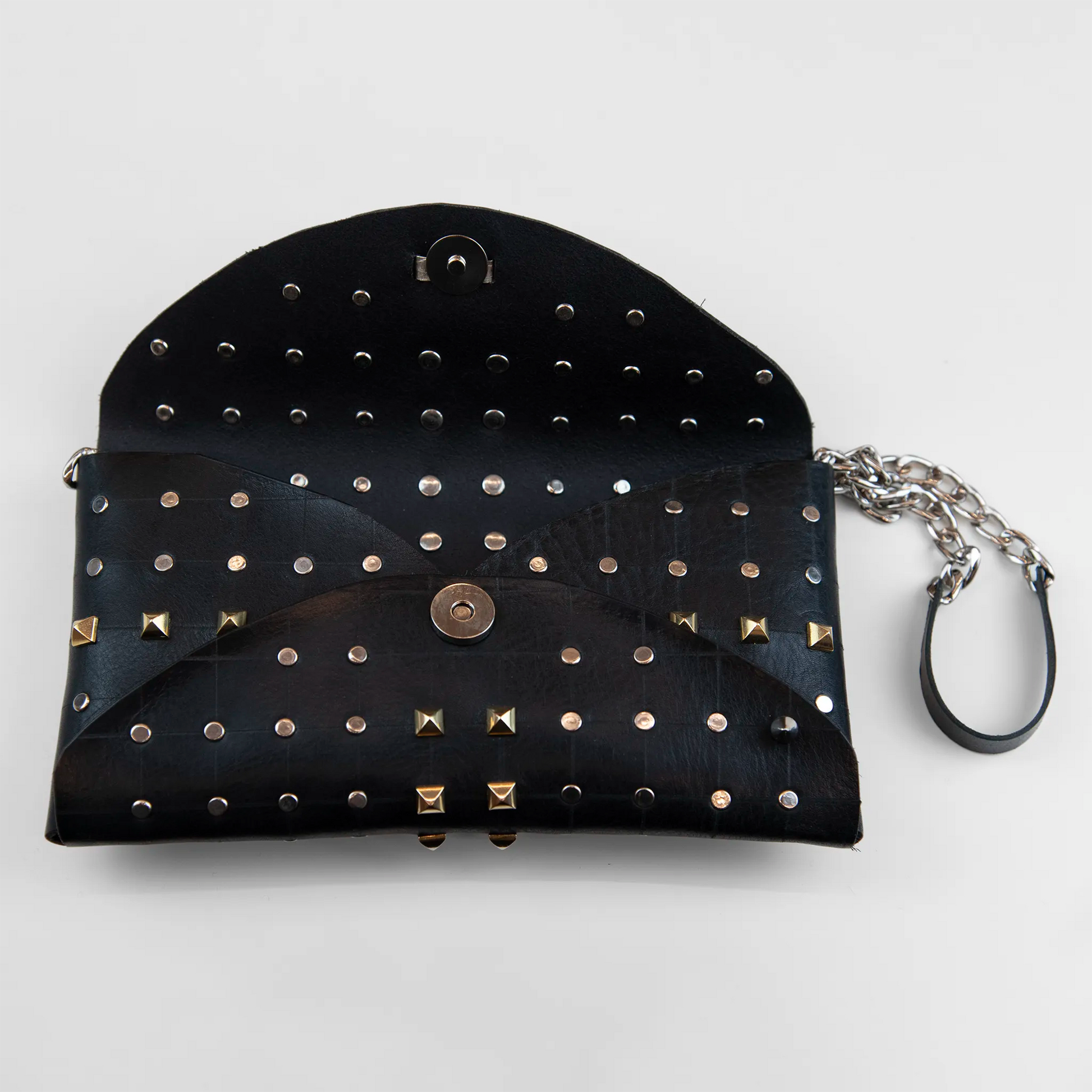 Clutch in pelle nera borchiata con chiusura a calamita, polsiera e tracolla, Made in Italy, realizzata interamente a mano senza cuciture, secondo la tradizione degli antichi sellai Toscani, per garantire robustezza e durata nel tempo.