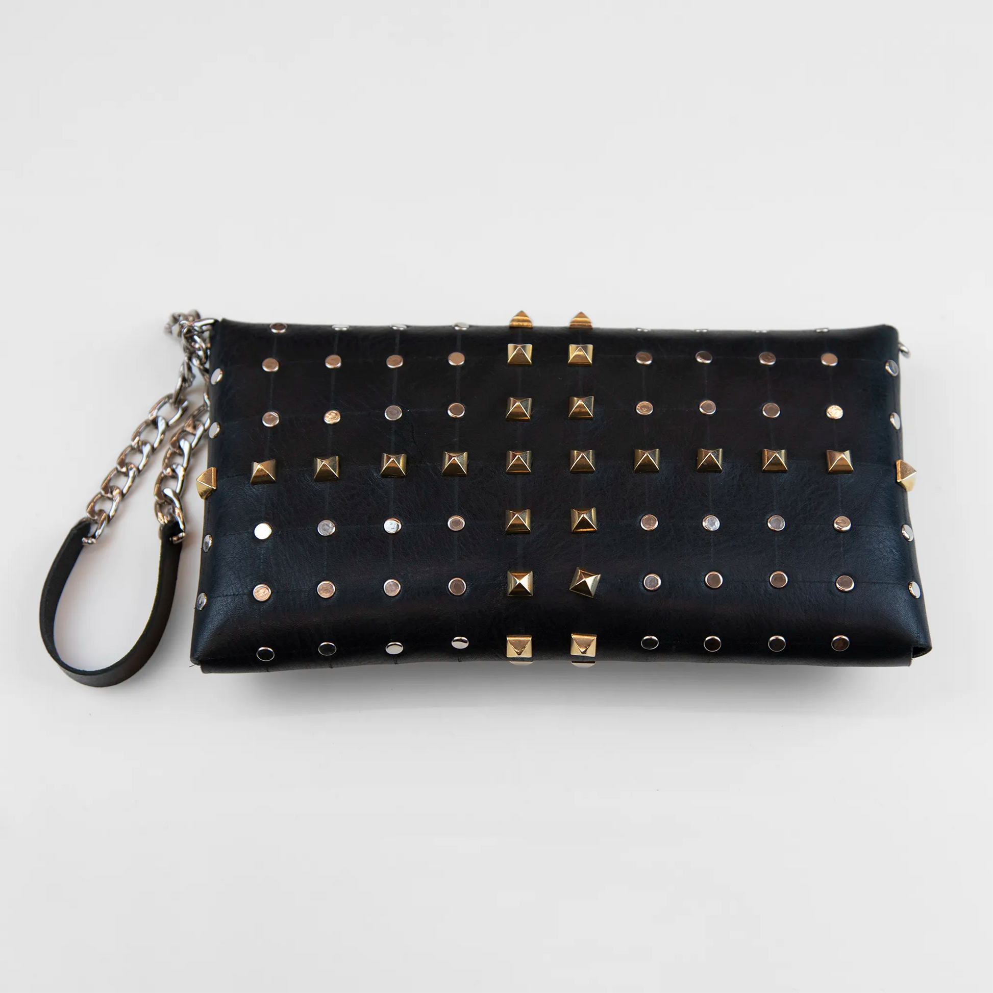 Clutch in pelle nera borchiata con chiusura a calamita, polsiera e tracolla, Made in Italy, realizzata interamente a mano senza cuciture, secondo la tradizione degli antichi sellai Toscani, per garantire robustezza e durata nel tempo.