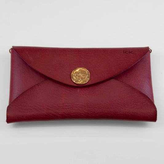 Clutch in pelle rossa con chiusura a calamita, polsiera e tracolla, Made in Italy, realizzata interamente a mano senza cuciture, secondo la tradizione degli antichi sellai Toscani, per una maggiore robustezza e durata nel tempo.